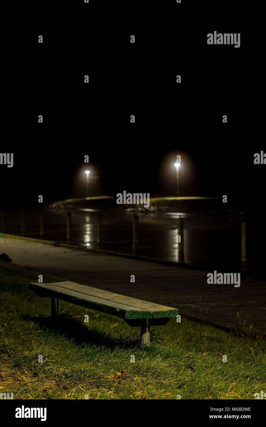 Nightphoto of bench with lights in background Stock Photo