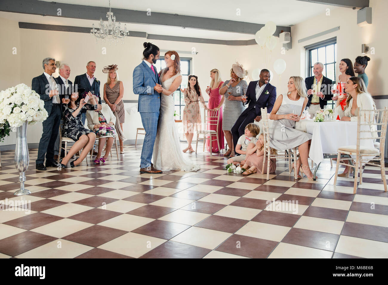 Beautiful couple are sharing their first dance on their wedding day. All of their guests are sitting around the dancefloor watching them. Stock Photo