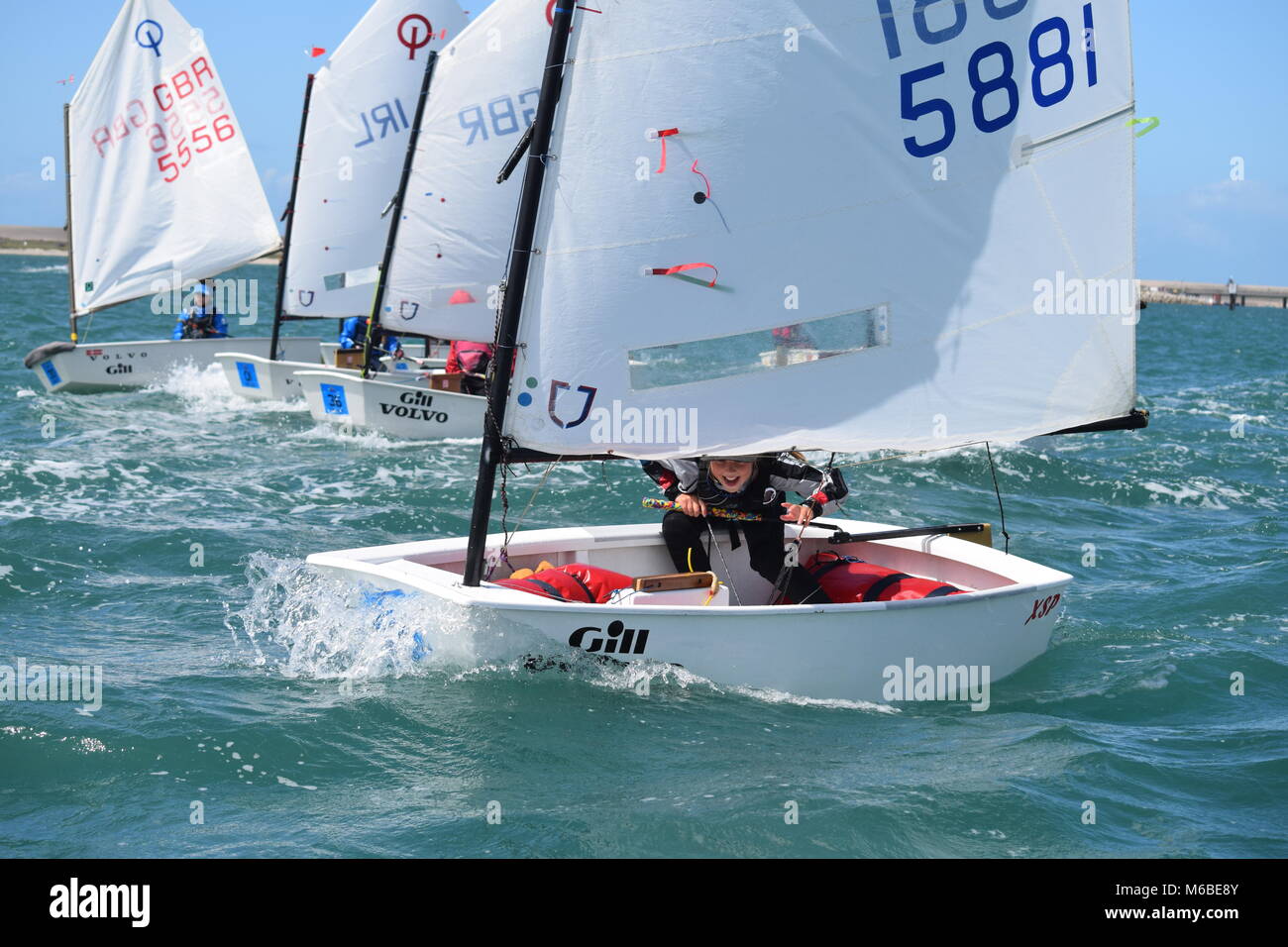 Junior sailors racing Optimist dinghies in Weymouth harbour on a sunny, windy day. Stock Photo