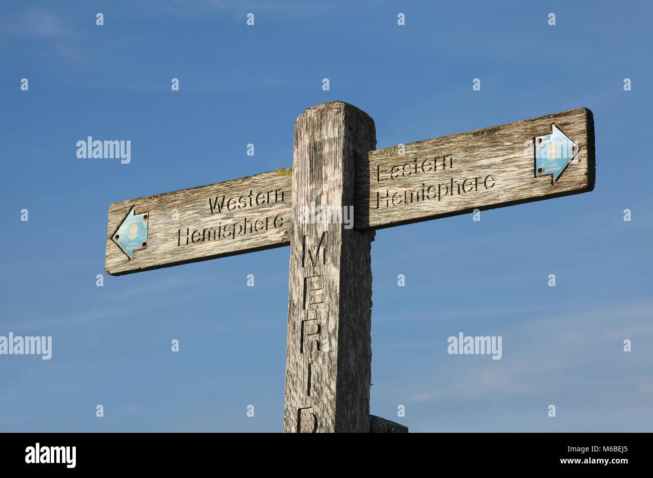 A wooden signpost on the South Downs marking the Greenwich Meridian. It points left to the 'Western Hemisphere' and right to the 'Eastern Hemisphere'. Stock Photo