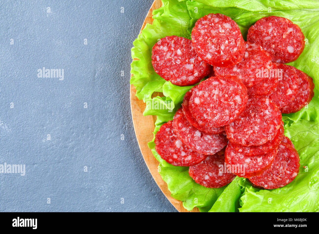 Smoked sausage, salami chopped in slices on a salad on a wooden circular cutting board on a concrete gray table Stock Photo