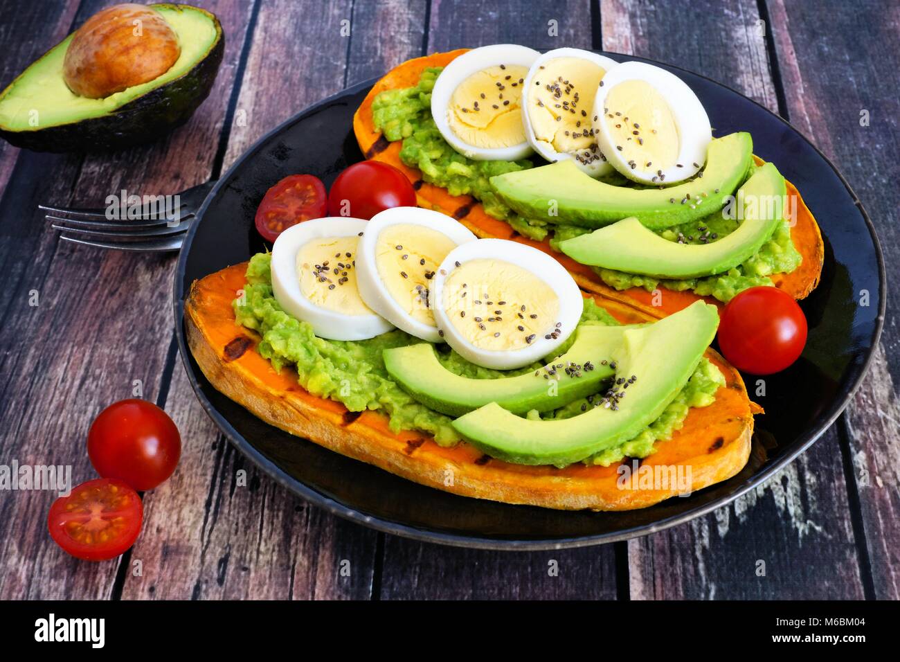 Sweet potato toasts with avocado, eggs and chia seeds on a dark plate. Table scene with a wooden background. Stock Photo