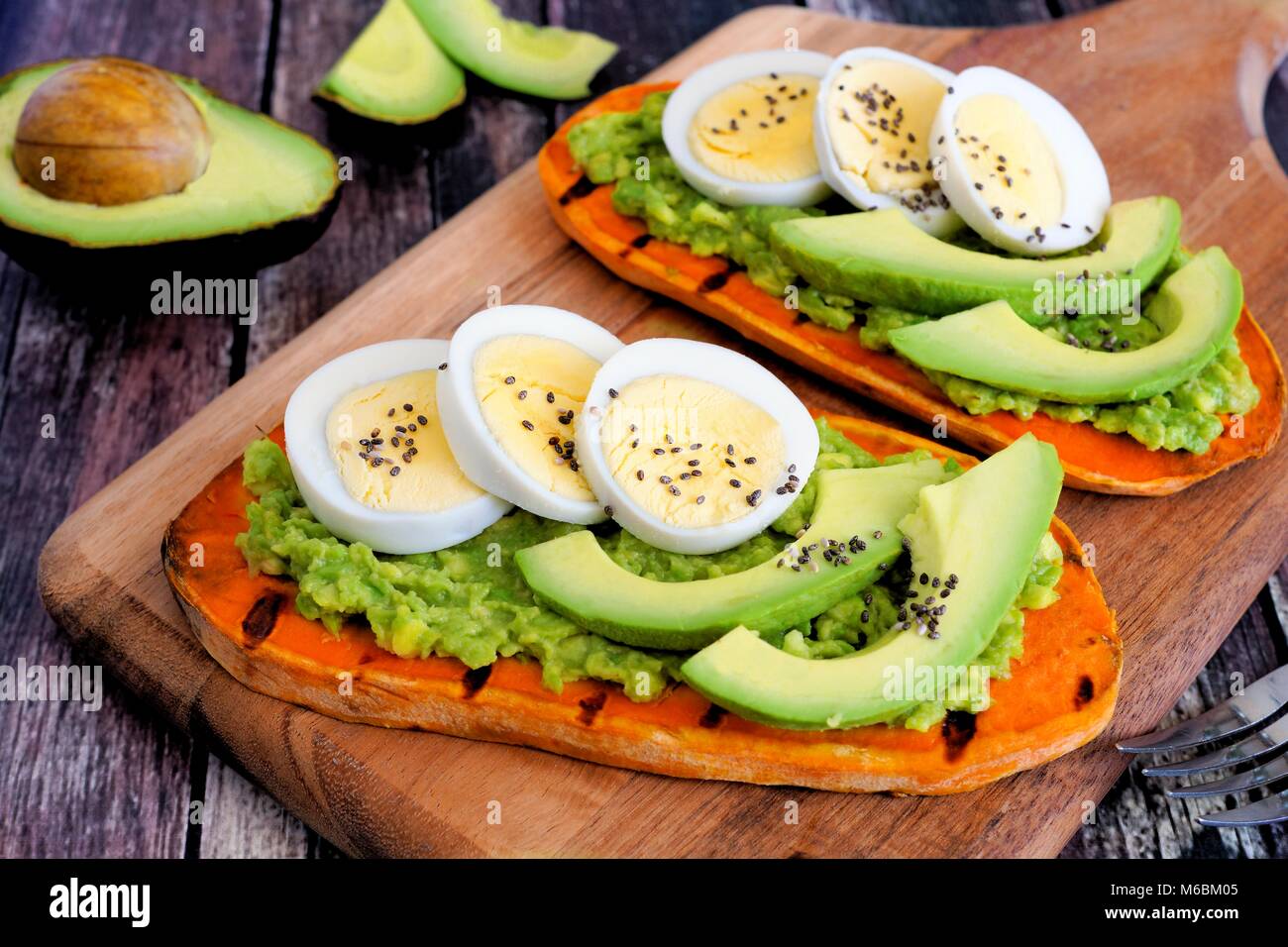 Sweet potato toasts with avocado, eggs and chia seeds on a wood board. Table scene with a wooden background. Stock Photo
