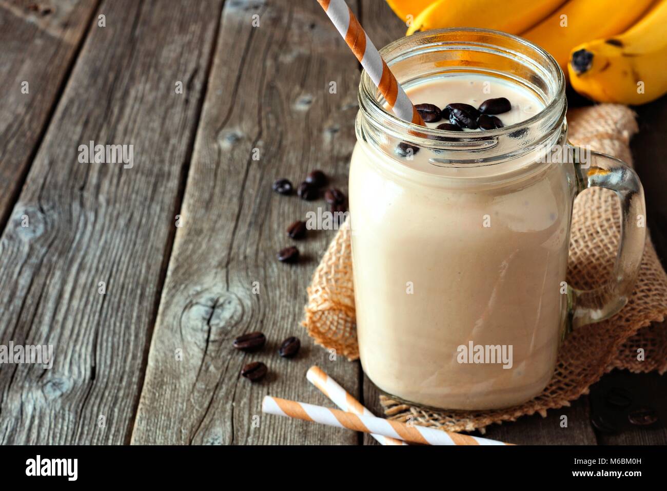 Coffee, banana smoothie in a mason jar. Side view with copy space over a rustic wood background. Stock Photo