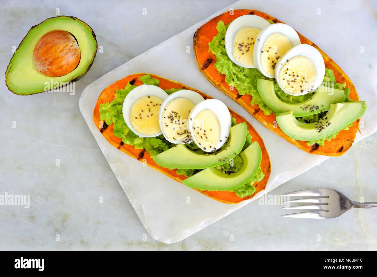 Sweet potato toasts with avocado, eggs and chia seeds on a marble server. Top view on a bright background. Stock Photo