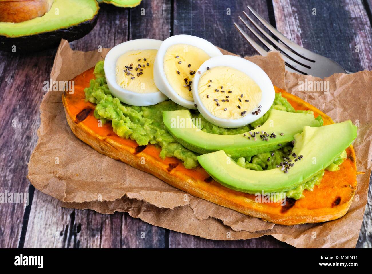 Sweet potato toast with avocado, eggs and chia seeds. Table scene with a wooden background. Stock Photo