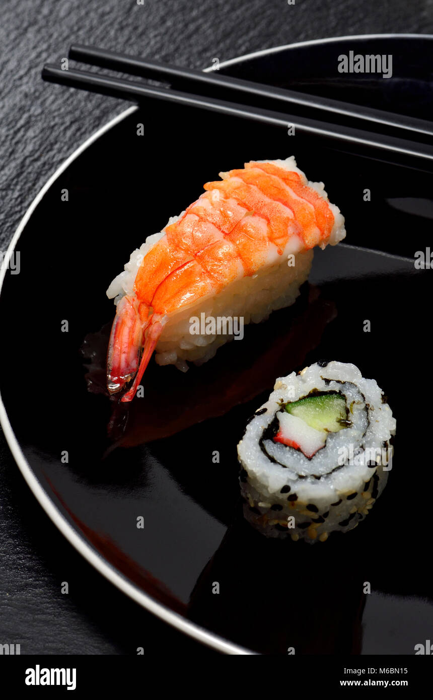 Sushi on a black plate: Nigiri (fish served on top of rice) uramaki (roll with rice on the outside) and chopsticks Stock Photo