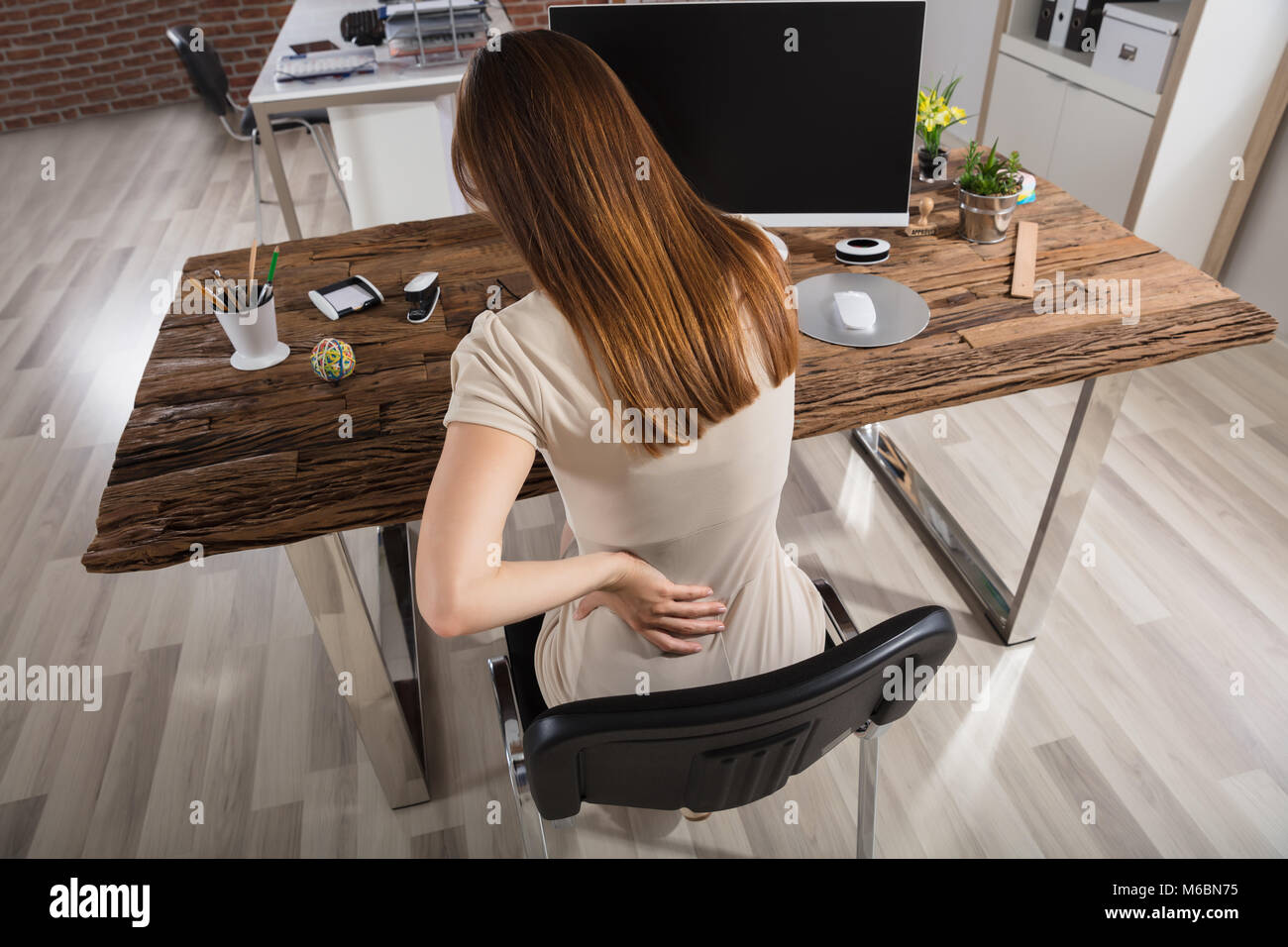 Young Businesswoman Having Back Pain Sitting On Chair At Workplace
