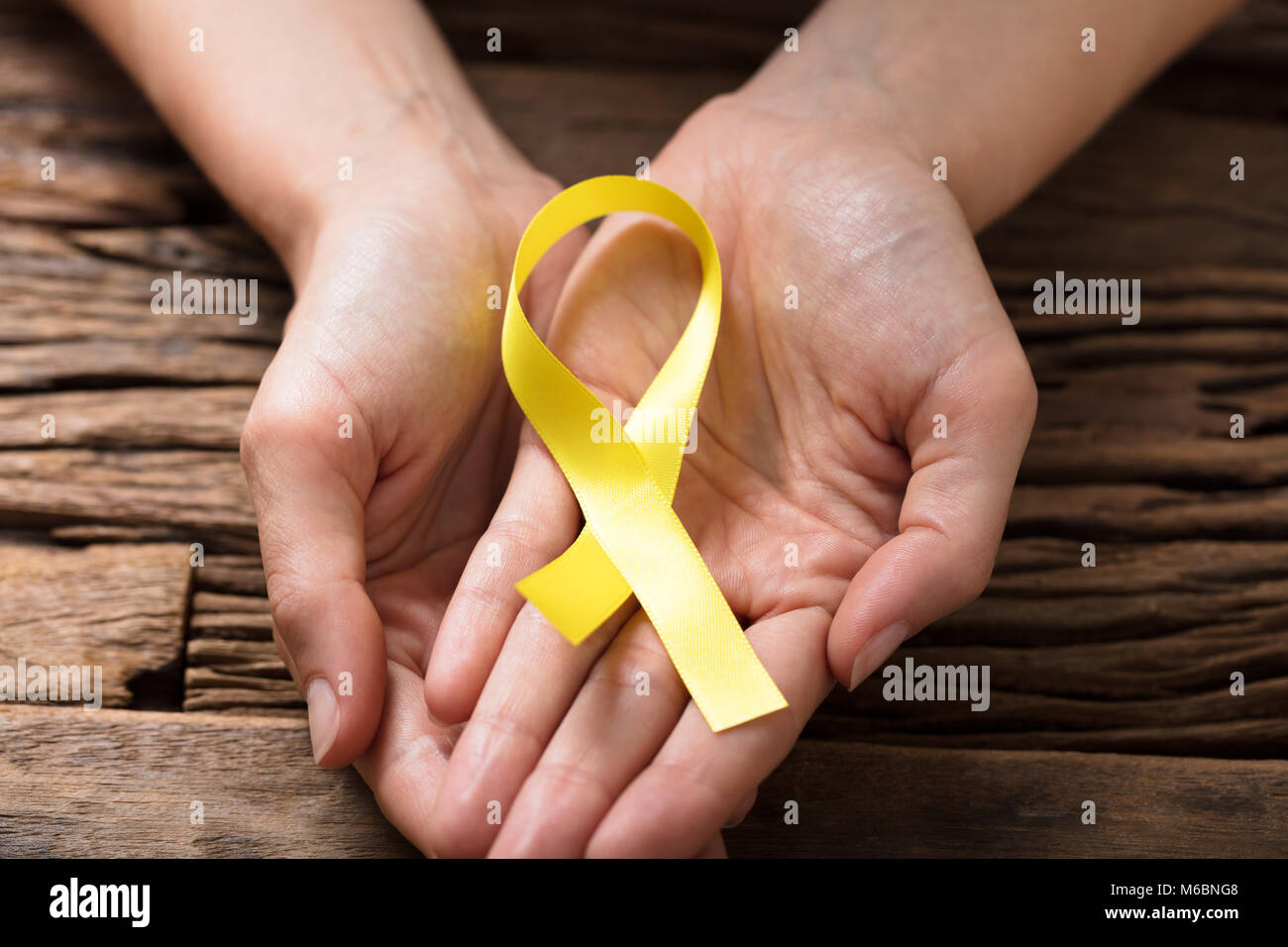 Close-up Of A Human Hand Showing Gold Ribbon To Support Childhood And Bladder Cancer Stock Photo