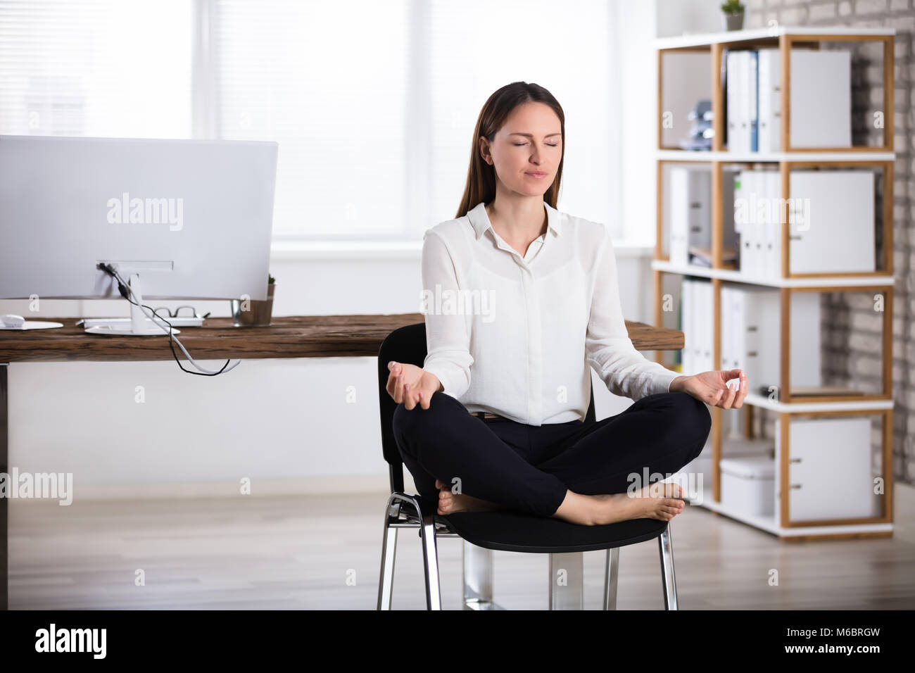 Young Businesswoman Sitting On Chair Doing Meditation Stock Photo