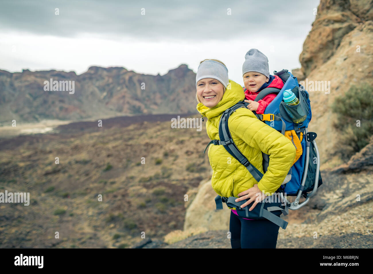 Happy mother with little boy travelling in backpack. Hiking adventure with child on autumn family trip in mountains. Vacations journey with infant car Stock Photo