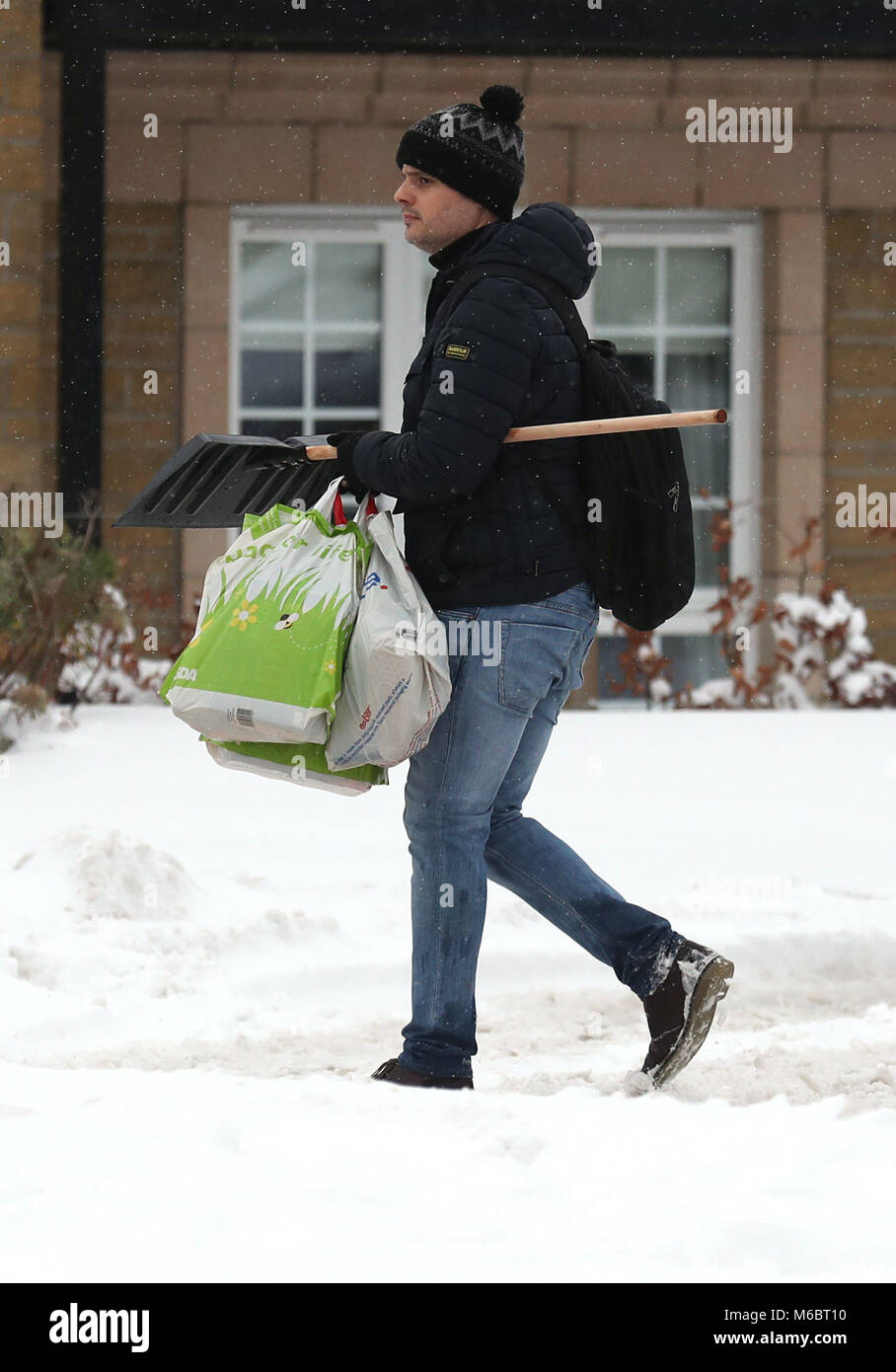 A man carries a snow shovel and shopping in Larbert, near Falkirk, as roads and railways have been rendered impassable by the coldest start to March on record, stranding hundreds of people in treacherous conditions. Stock Photo