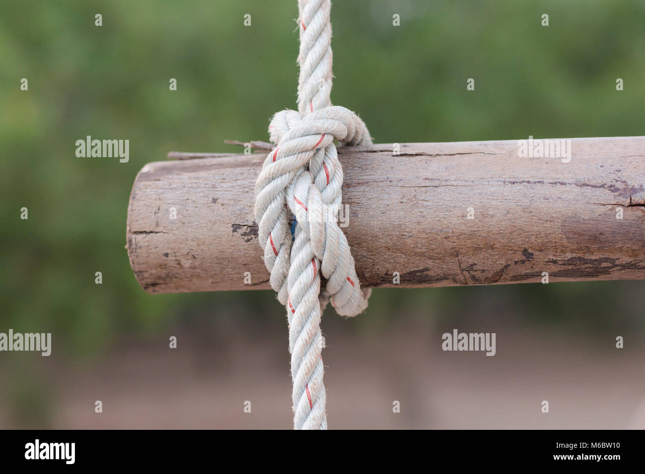 A rope is tied in a knot around a fence post , rope tied knot wood pole