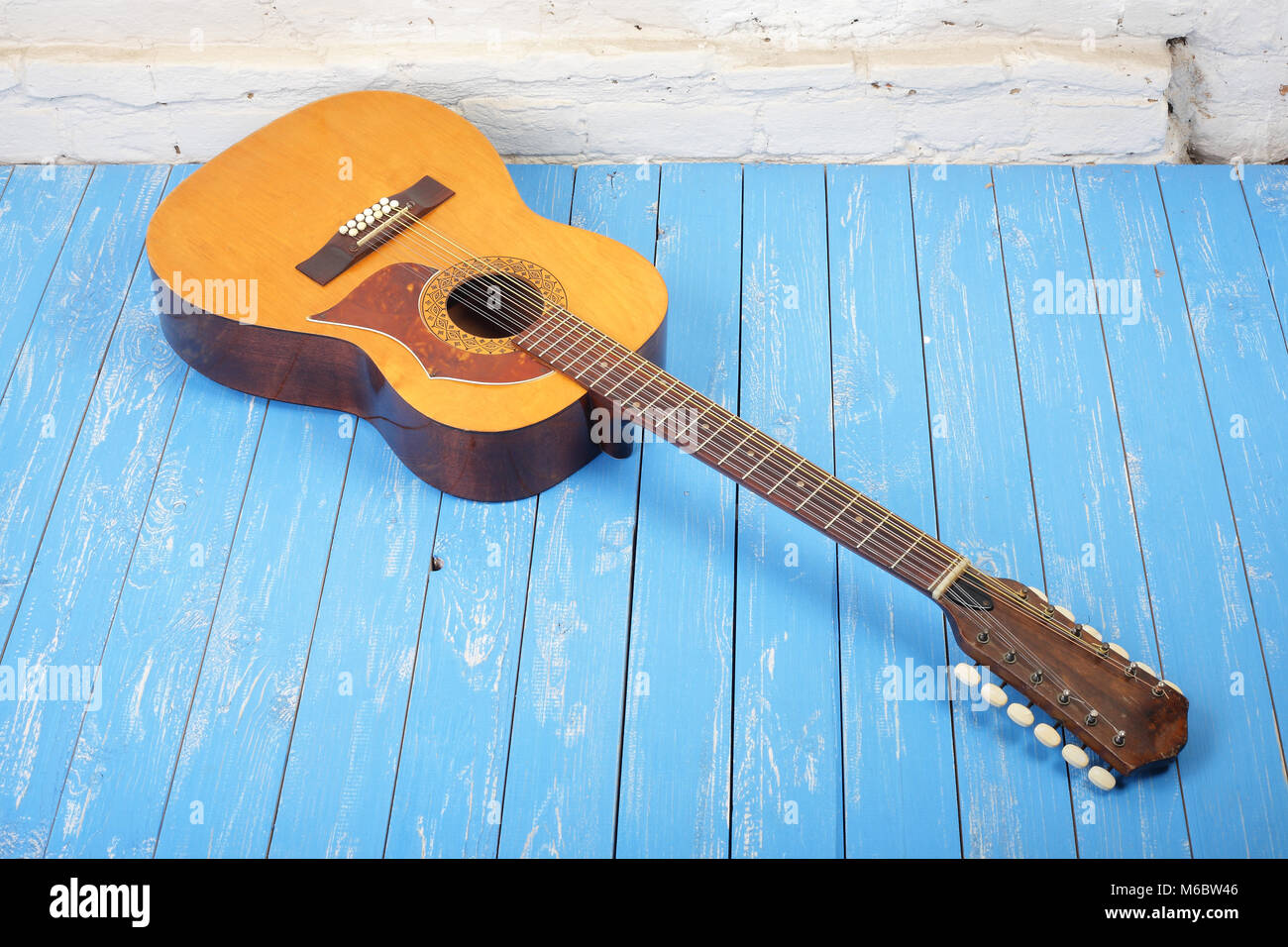 Musical instrument - Vintage twelve-string acoustic guitar on a brick background and blue wooden floor. Stock Photo