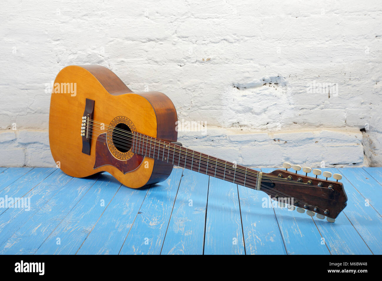 Musical instrument - Vintage twelve-string acoustic guitar on a brick background and blue wooden floor. Stock Photo