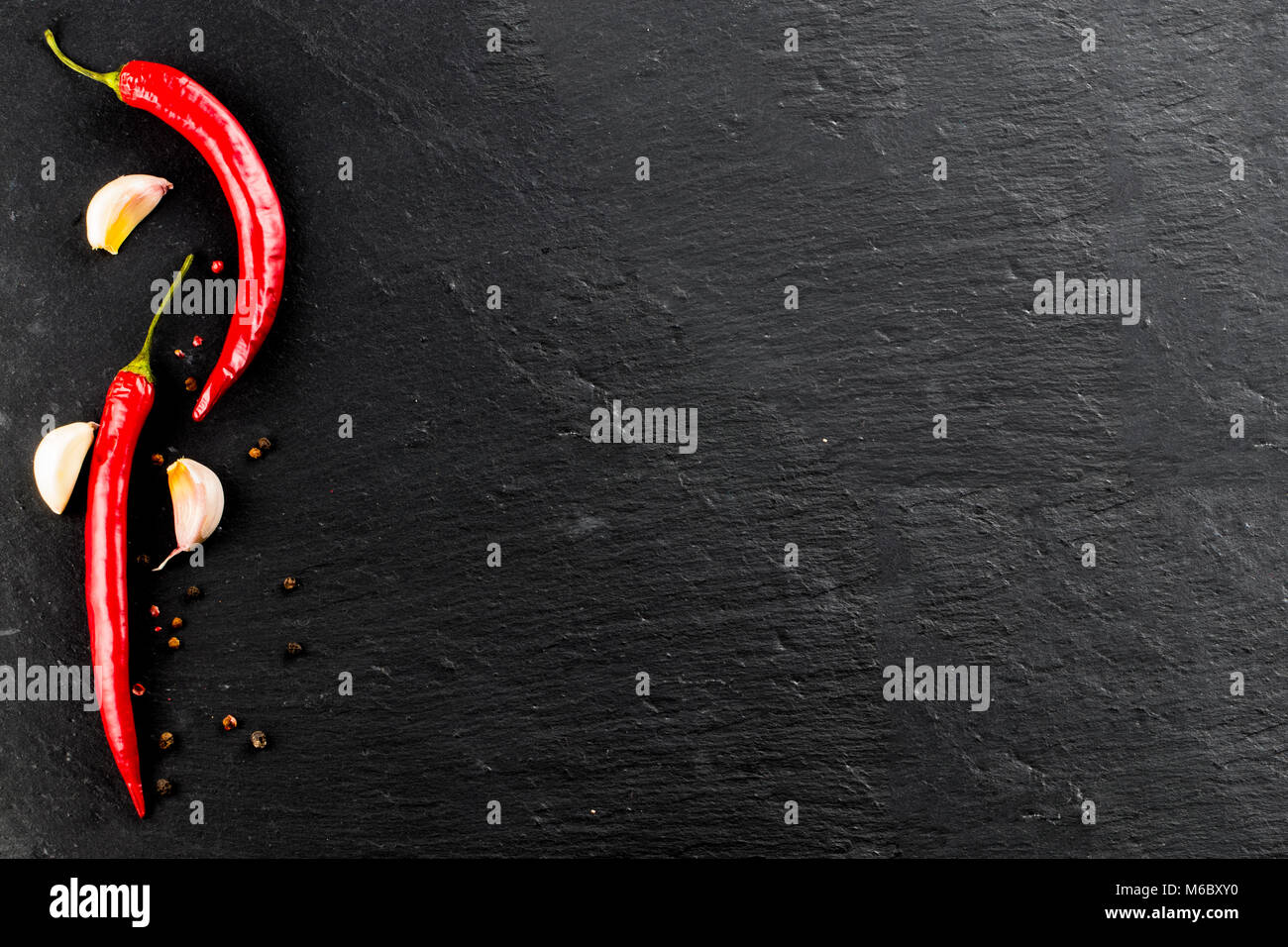 Red hot chili peppers and peppercorns on black background, top view