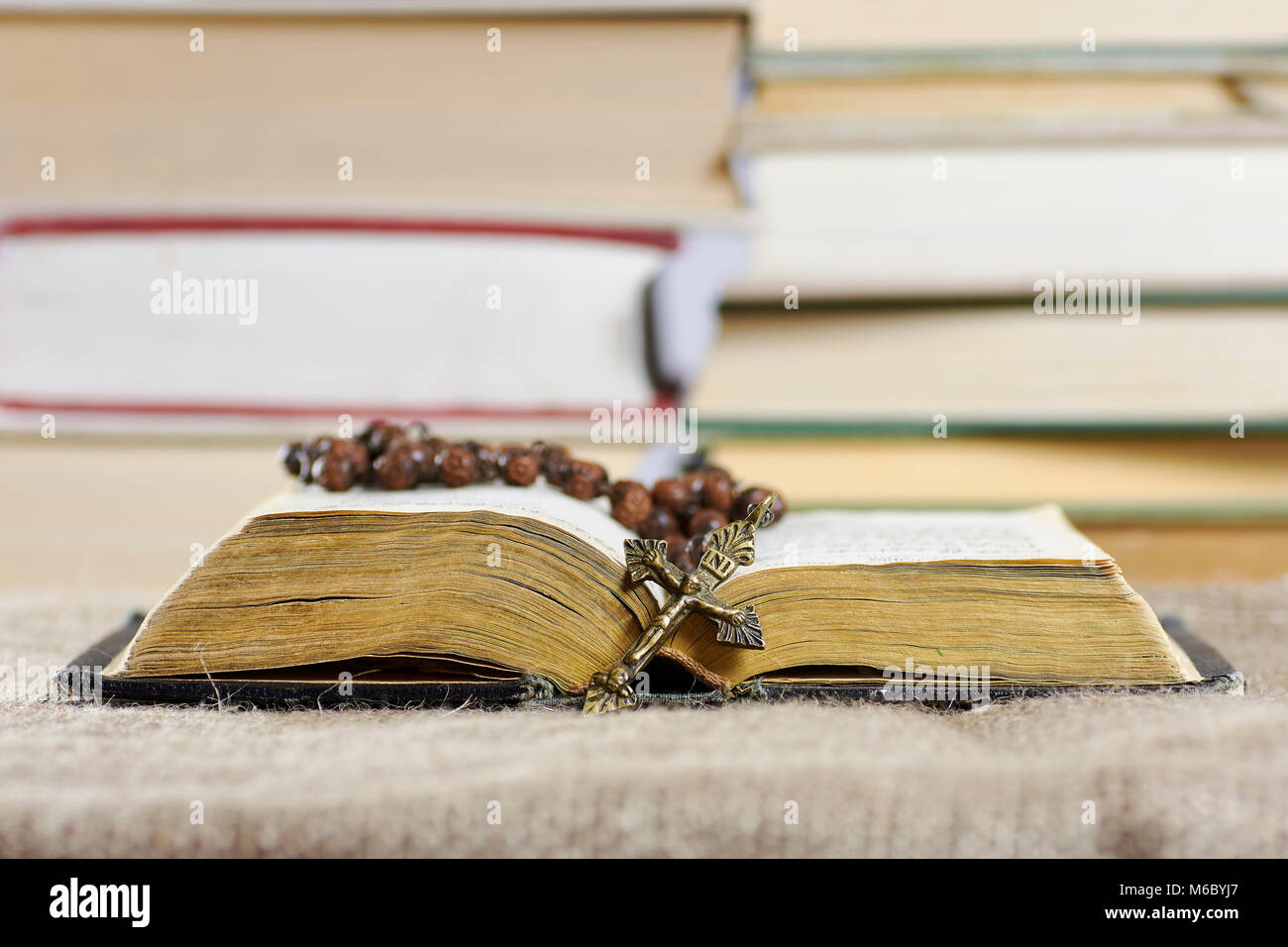 An open old book with a rosary in a hard cover with blurred books in the background Stock Photo