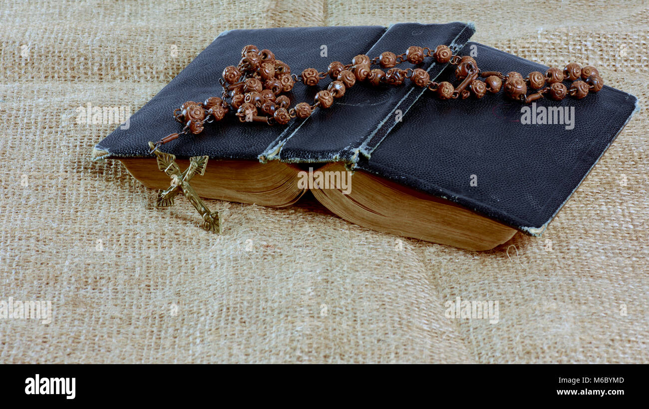 An open old book with a rosary in a hard cover lying on the jute Stock Photo