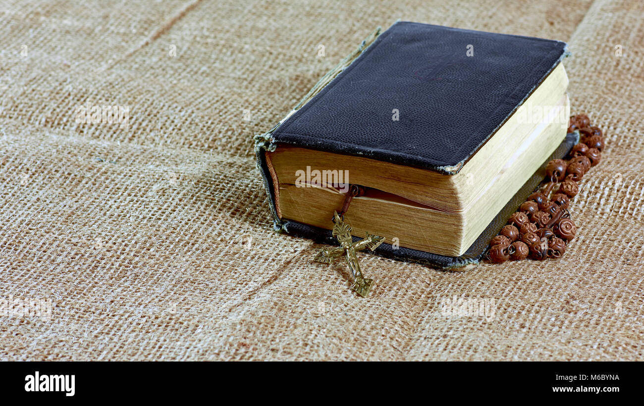 A closed old book with a rosary in a hard cover lying on a jute Stock Photo