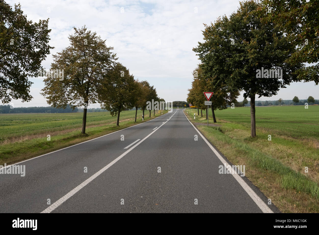 German country road in autumn near Leipzig with fields to its sides and a junction approaching, hence the give way streetsign Stock Photo