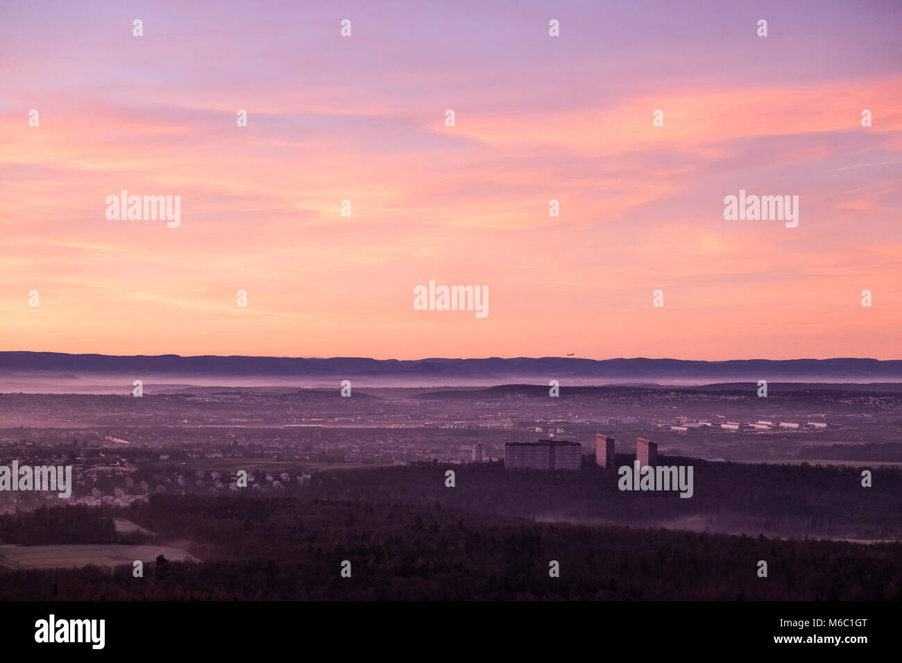 Aerial view of the city of Stuttgart towards the swabian alb with an airplane starting in a beautiful morning sunrise as seen from the tv tower (Fernsehturm) of the city. Stock Photo