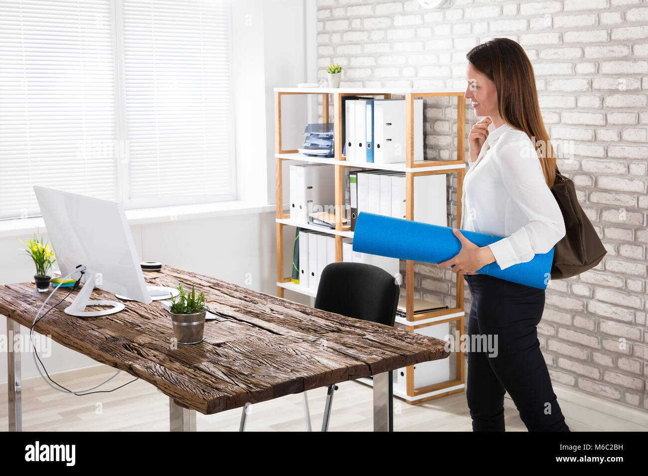 Happy Young Businesswoman Walking In Office With Exercise Mat Near