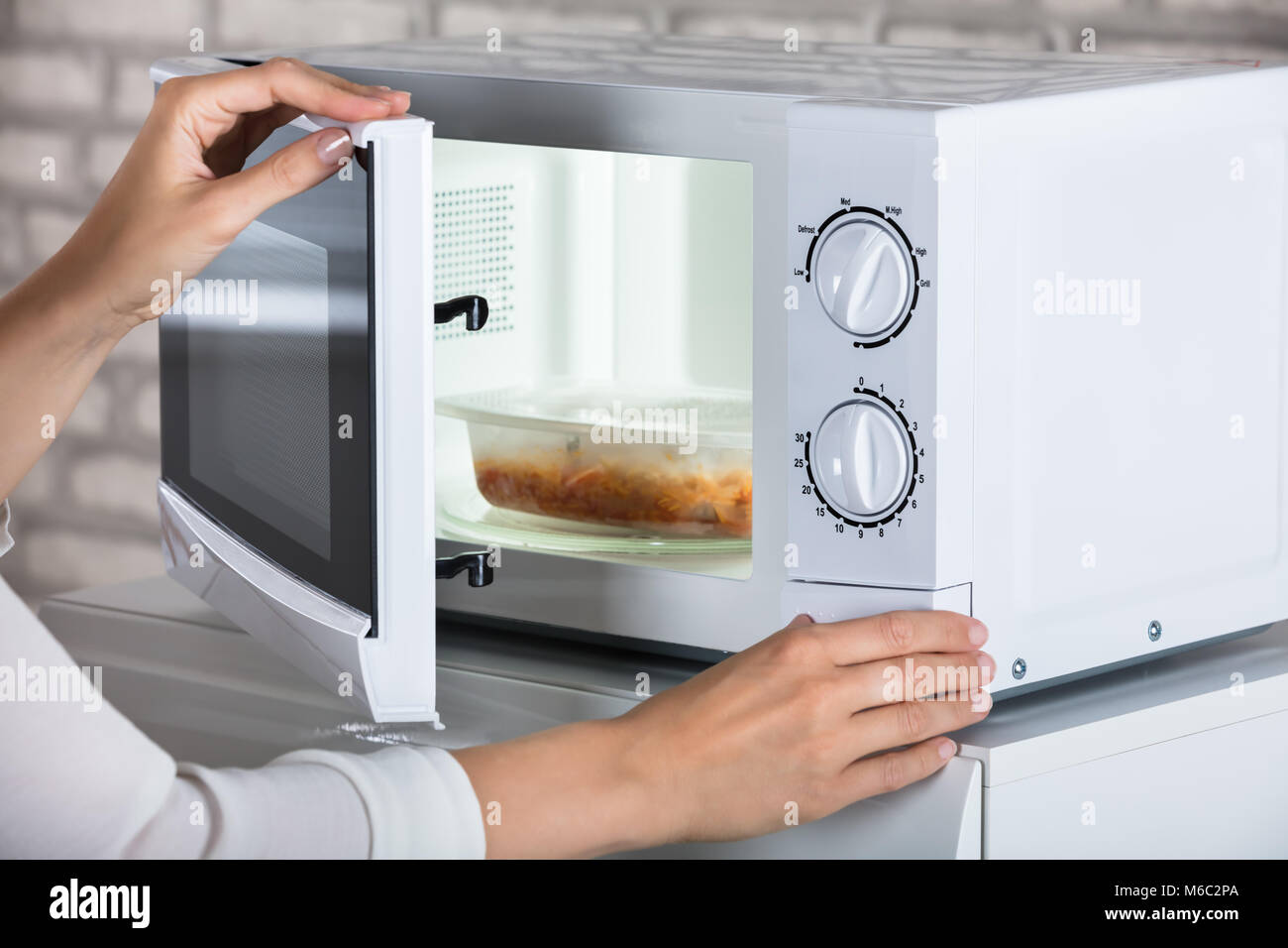 Woman's Hands Closing Microwave Oven Door And Preparing Food At Home Stock Photo