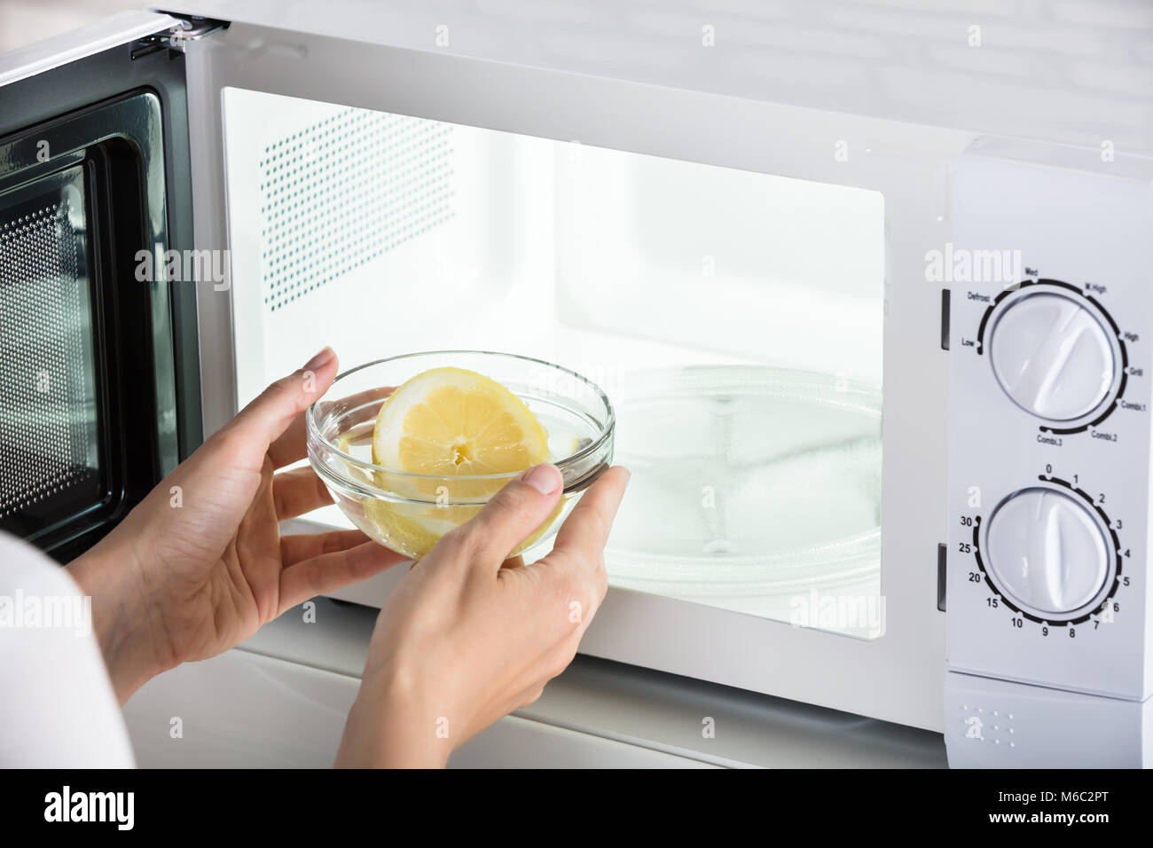 Close-up Of Woman Putting Bowl Of Slice Lemon In Microwave Oven Stock Photo