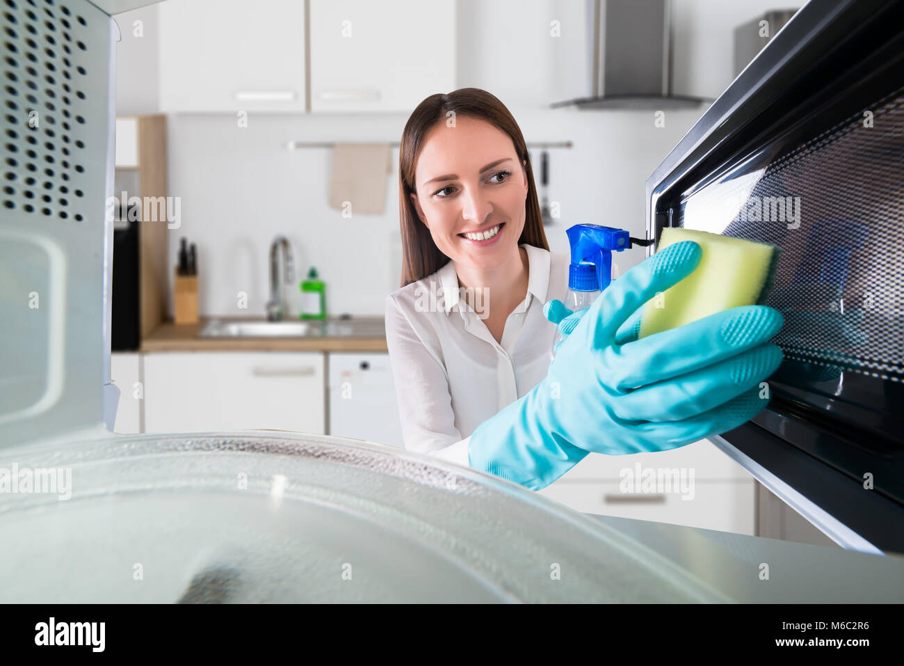 Young Woman Cleaning Microwave Oven With Spray Bottle And Sponge Stock Photo