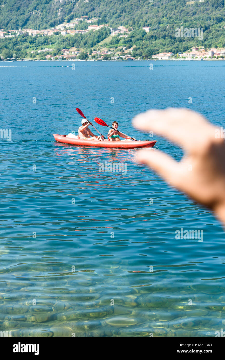 Lago d'Orta, Italy - August 12, 2016: A hand seems to be grabbing a canoe with two elderly people paddling on the Lake Orta - Lago d'Orta in Italy. Stock Photo