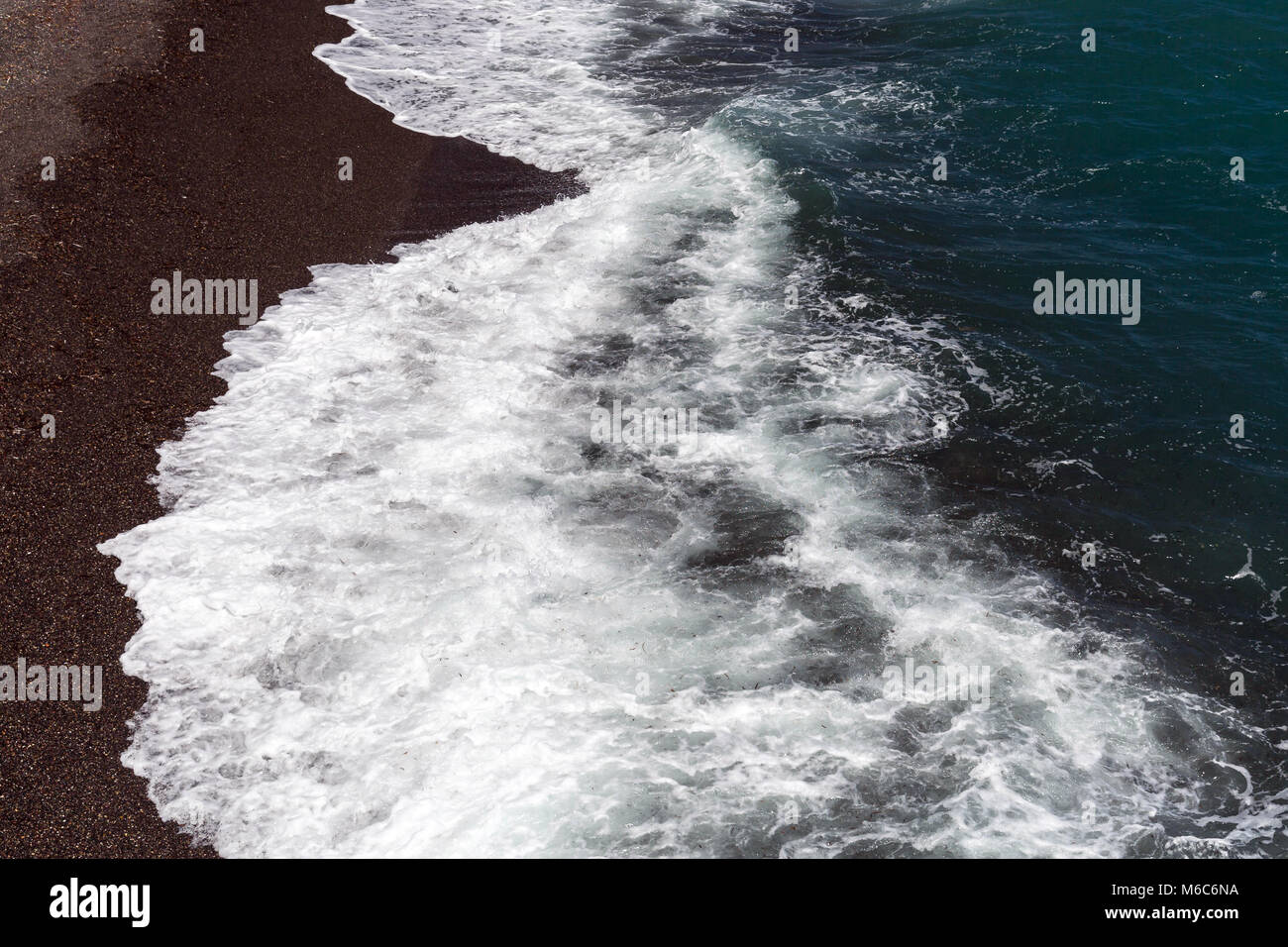 Waves with white foam on dark volcanic beach Stock Photo - Alamy