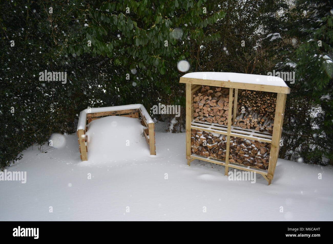 log store with a mono pitch roof in garden made from treated wood and compost heap formed of re-used pallets covered with heavy snowfall Stock Photo