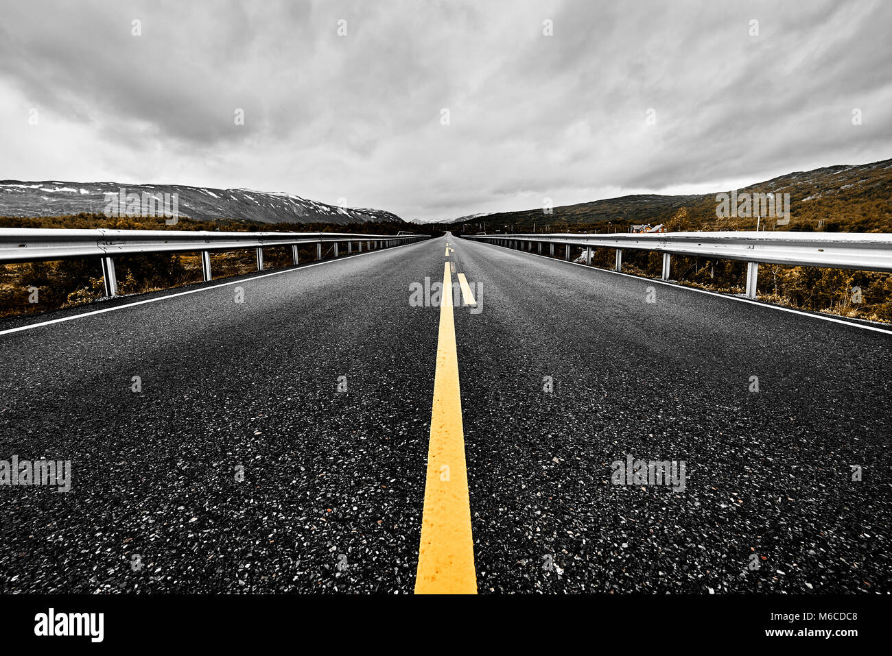 image of a wide open prairie and mountains with a paved highway road stretching out as far as the eye can see with beautiful nature under a cloudy sky Stock Photo
