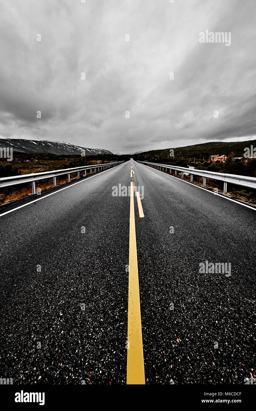 image of a wide open prairie and mountains with a paved highway road stretching out as far as the eye can see with beautiful nature under a cloudy sky Stock Photo