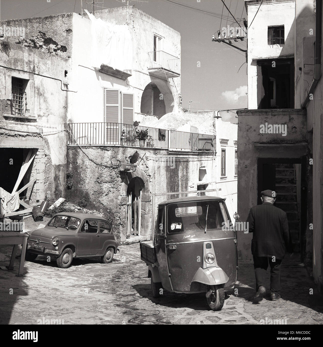 1950s, historical, summertime and a tight narrow sidestreet with Italian vehicles of the era, a small fiat 'bubble car' and a 'vespaCar', a three-wheeled delivery van, a Piaggio Ape 400, parked on the uneven cobbles, on the mediterranean island of Elba,Tuscany, Italy, Stock Photo