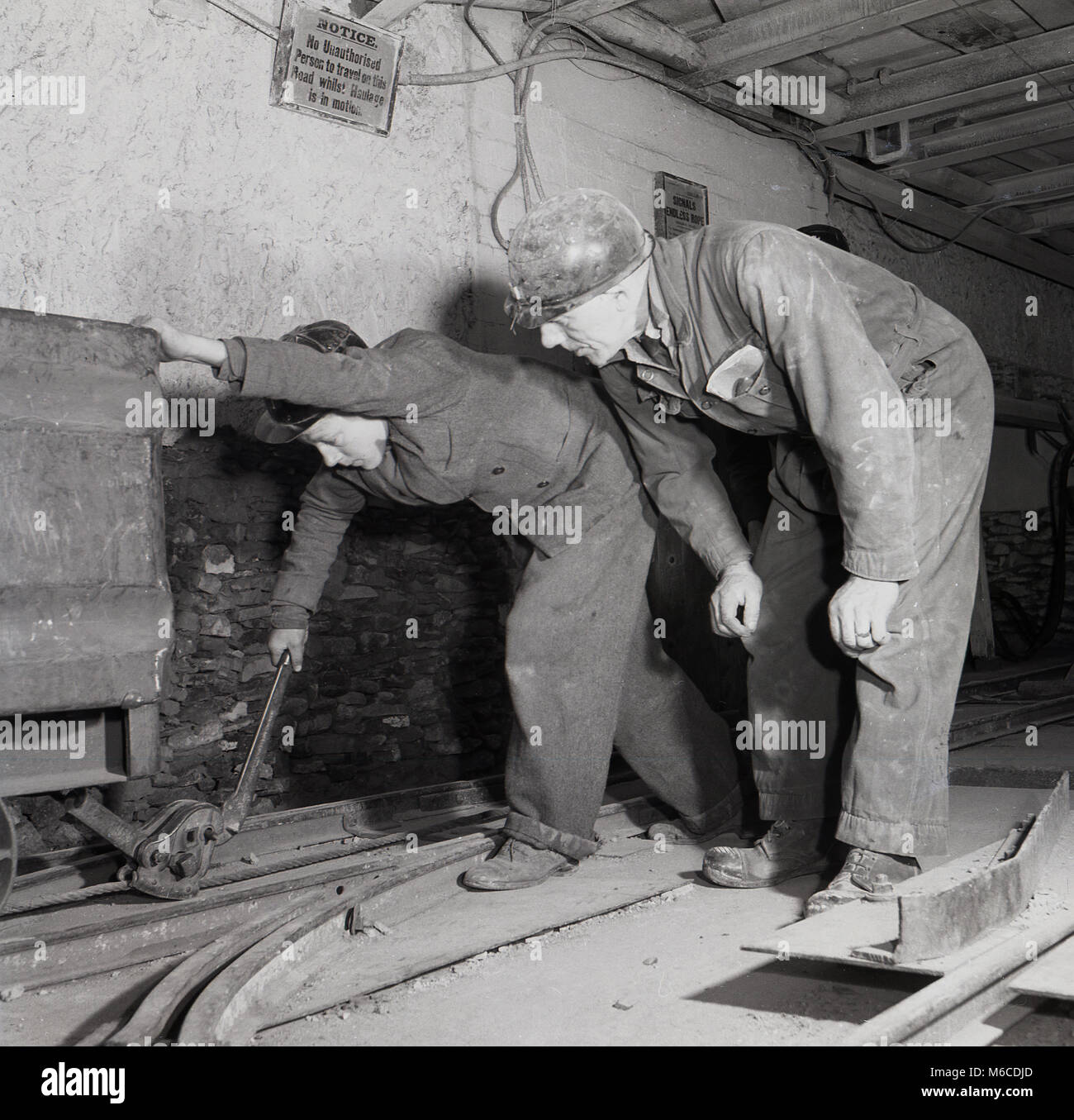 1950s, historical picture, a coal miner instructing a young male apprentice how to lock and unlock a mine trolley or minecart, England, UK Following WW2, there was a need to rebuild industry and infrastructure in Britain and so industrial apprenticeships in the field were important employment routes for many and were encouraged by the government of the day. At the time mining was a big industry in many parts of the UK, including Nottinghamshire, Derbyshire and South Yorkshire, and so many youngsters worked at the mines for the National Coal Board. Stock Photo