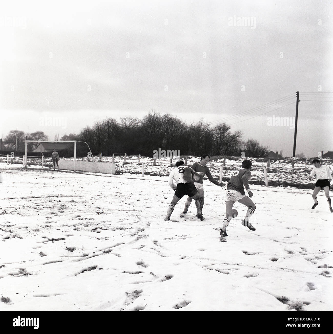 1960s, historical, wintertime and amateur footballers playing a game on a snow covered pitch, England,, UK. Stock Photo