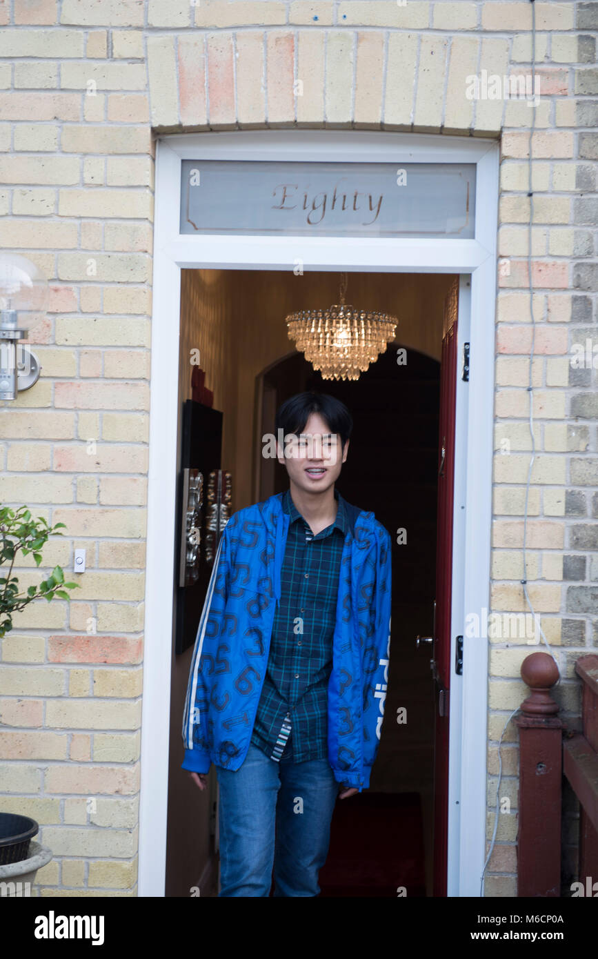 an asian student leaves his student accommodation through the front door Stock Photo