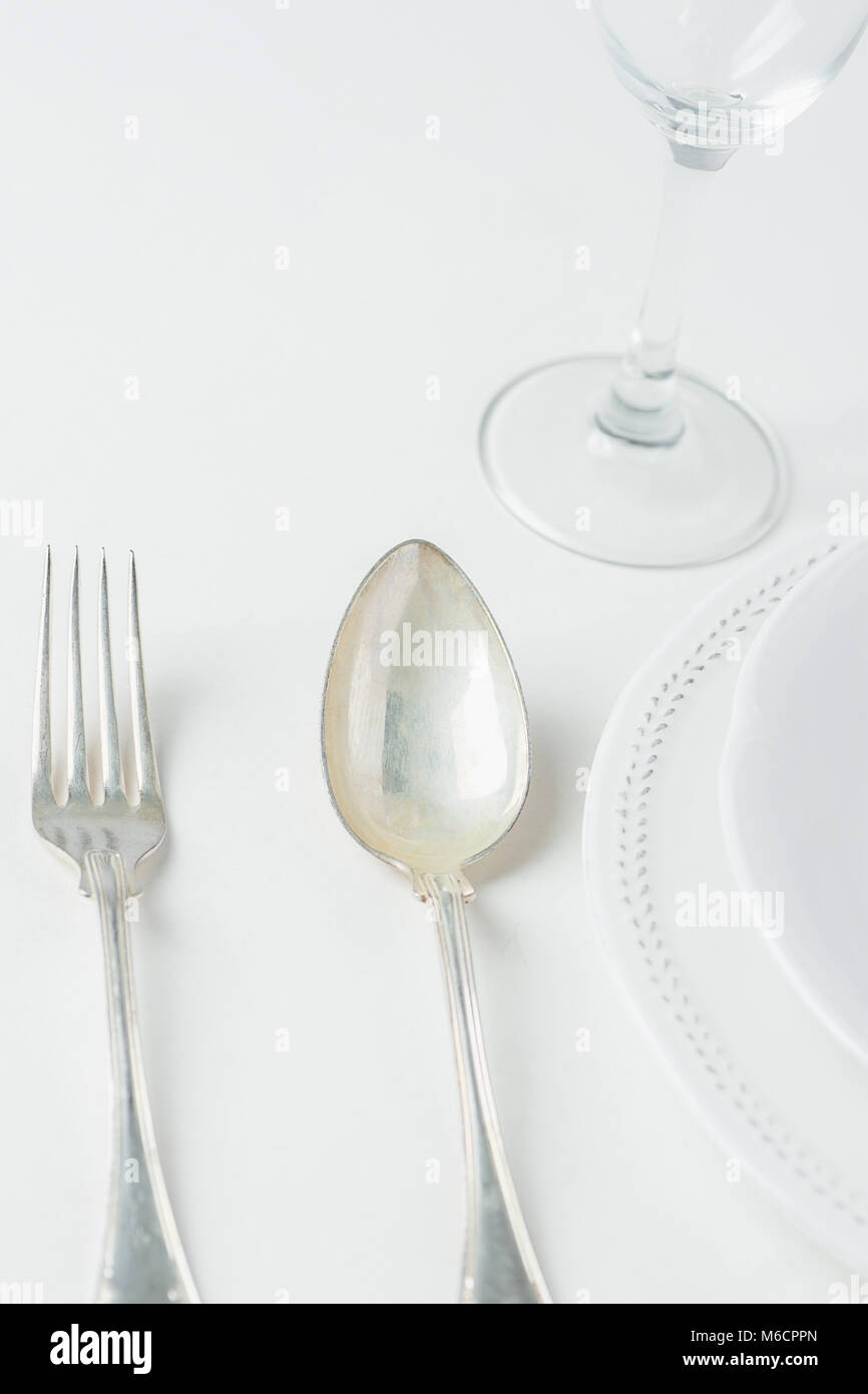 White Vintage Empty Plates Unpolished Silver Fork Spoon Wine Glass on Concrete Tabletop. Minimalist Japanese Style Table Setting. Template for Poster  Stock Photo