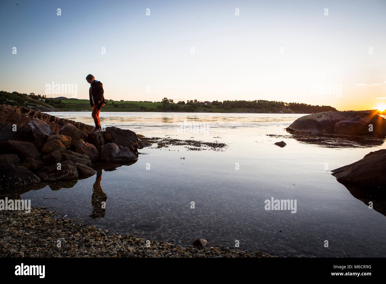 Woman strolling along the shore of a river in sunset. Stock Photo