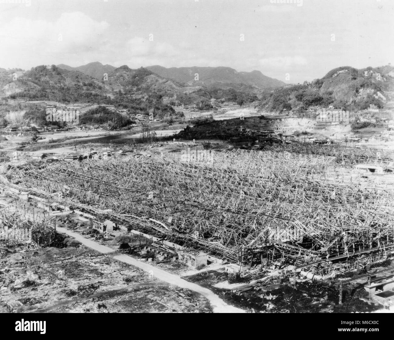 View of the stripped roof and distorted steel frame of the Mitsubishi Torpedo Works, located 4500 feet from ground zero at Nagasaki. Note intact buildings in the background, shielded by uneven terrain. Nagasaki, Japan, 1945. U.S. Air Force Stock Photo