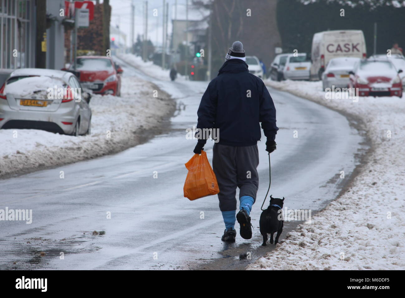 Llantwit Fardre, Pontypridd, Wales, UK - March 03 2018: A man walks his dog home from a store along a snowy, slushy street. Abandoned vehicles parked up on the side of the road in the background. Credit: Elizabeth Foster/Alamy Live News Stock Photo