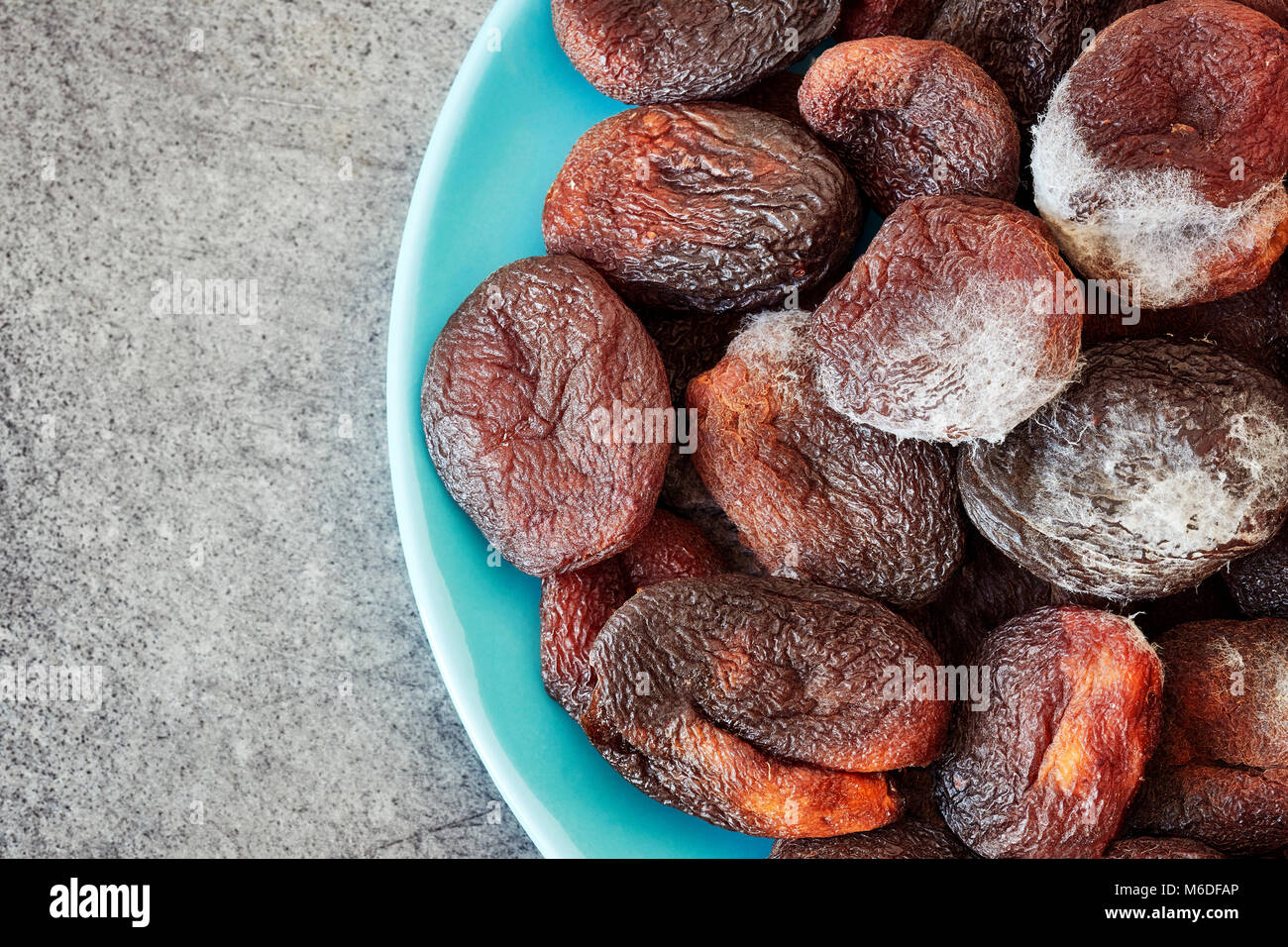 Moldy dried apricots on a plate, space for text. Stock Photo
