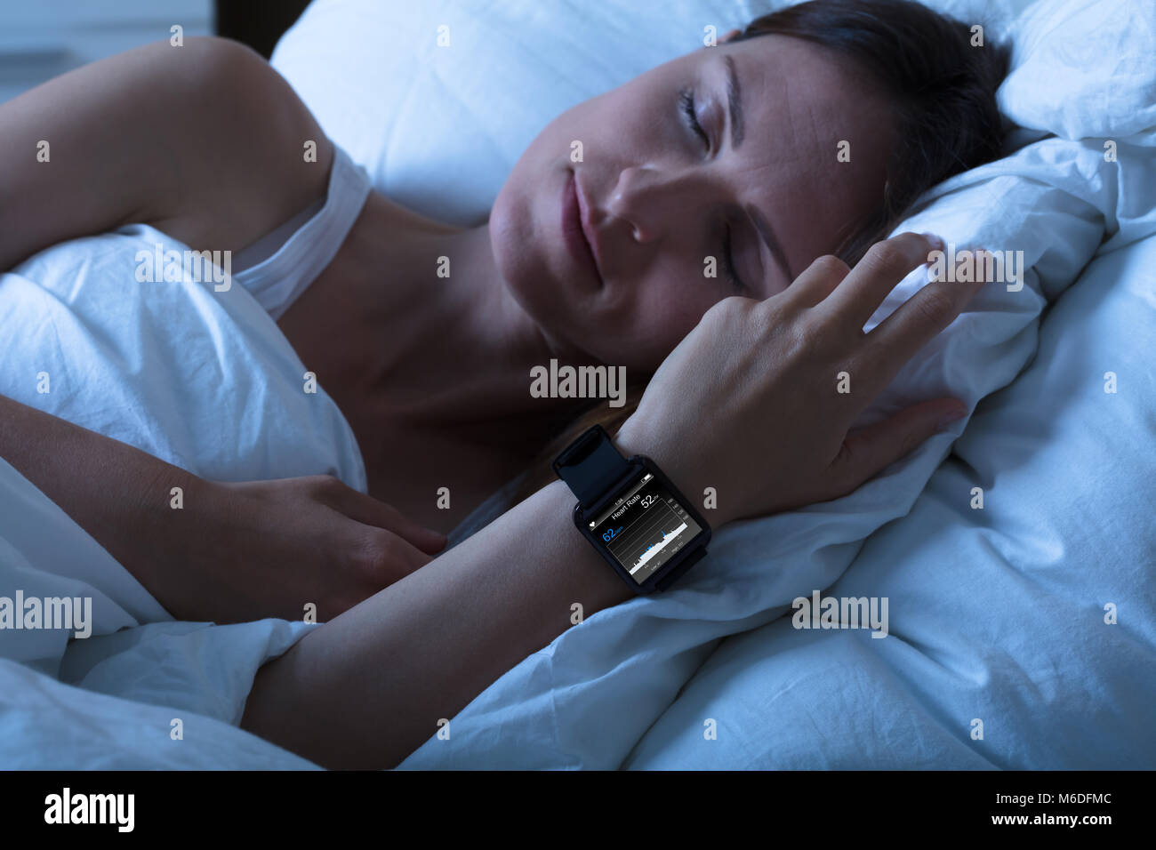 Close-up Of A Woman Sleeping With Smart Watch Showing Heartbeat Rate On Bed Stock Photo