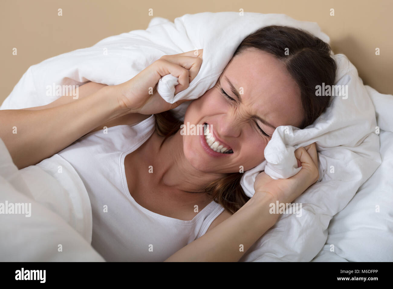 Troubled Woman In Bed Covering Ears To Shut Out Noise Stock Photo