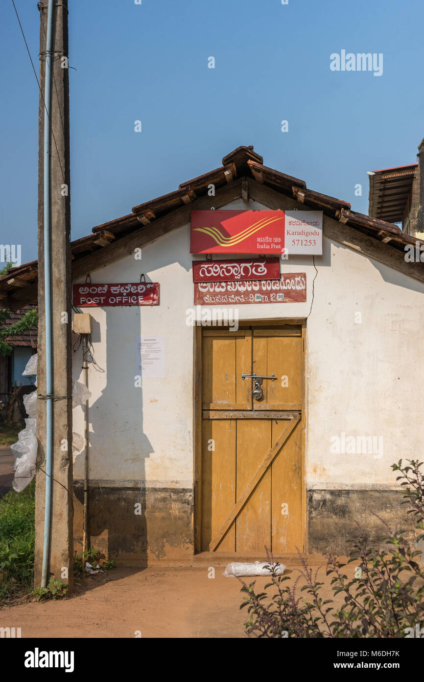 Madikeri, India - October 31, 2013: Public post office shows closed brown wooden door set in white wall under blue sky. Lightpost and red signs. Packa Stock Photo