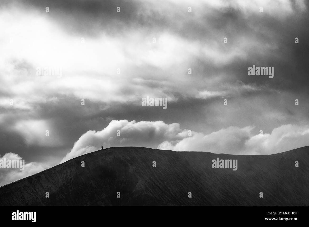 A black and white timeless capture of a person walking on the crater of massive Mount Bromo volcano under the heavy clouds Stock Photo