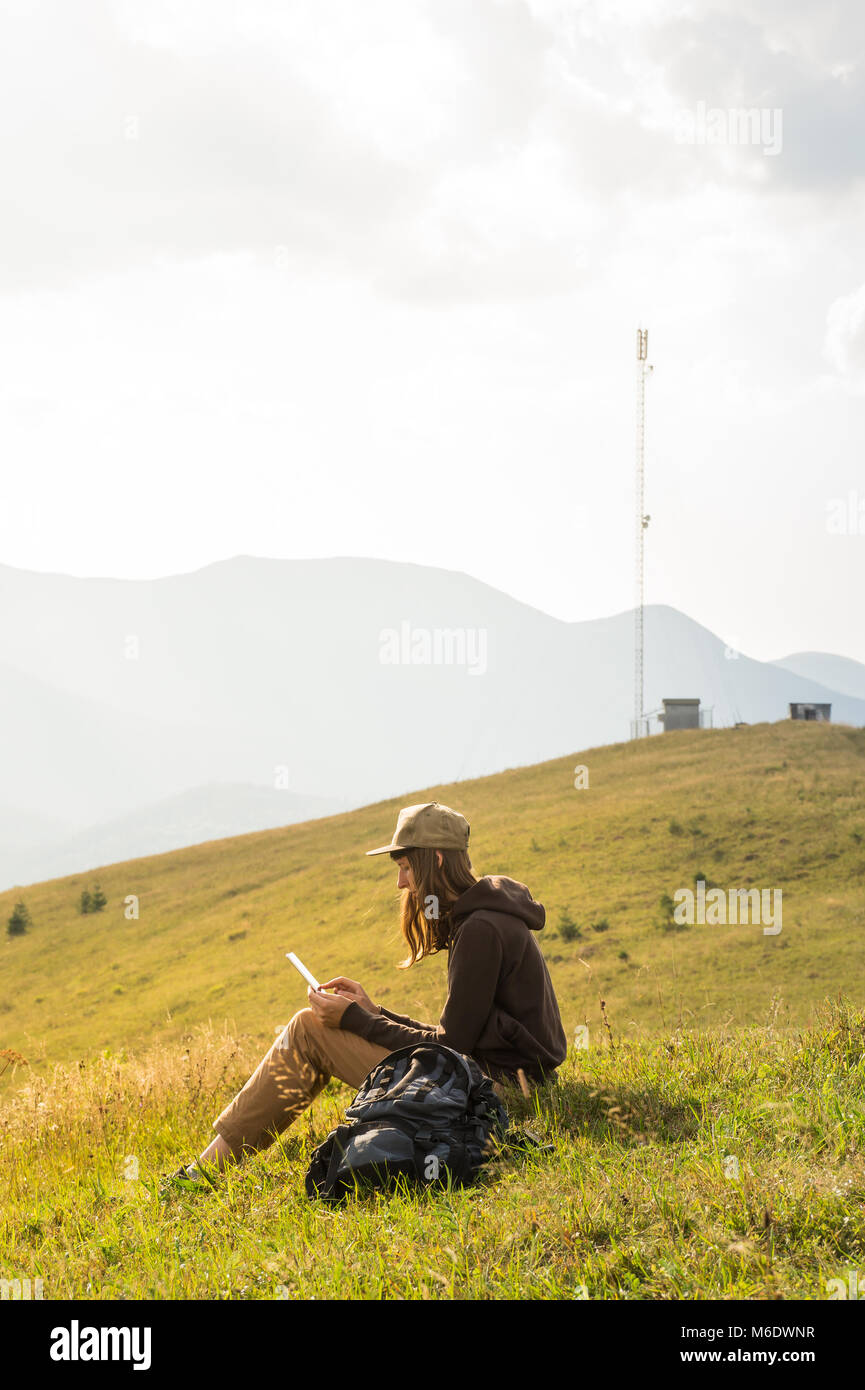 Young female sits in field outdoors and works on project online near mobile network base Stock Photo