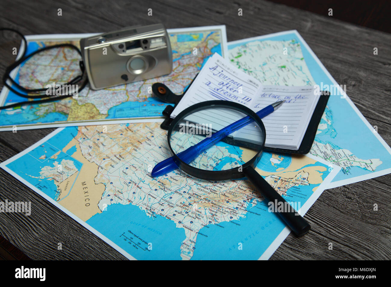 A person is preparing to travel. On the table are atlases of the United States. At the top there is a magnifying glass, a pen, a notebook with a recor Stock Photo
