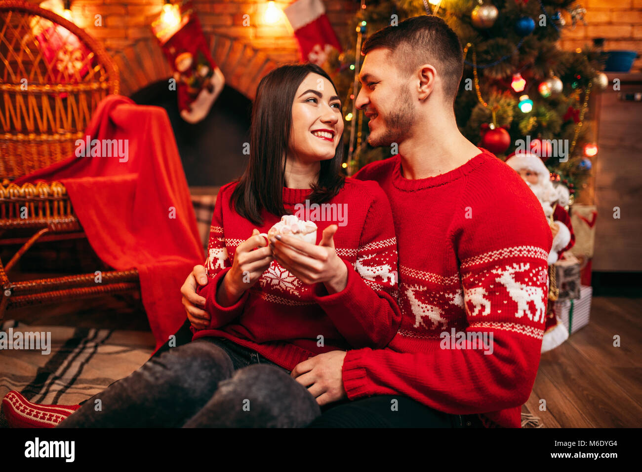 Love couple, romantic christmas celebration. Xmas holidays, man and woman sitting on the floor and drinks coffee with whipped cream, festive decoratio Stock Photo - Alamy